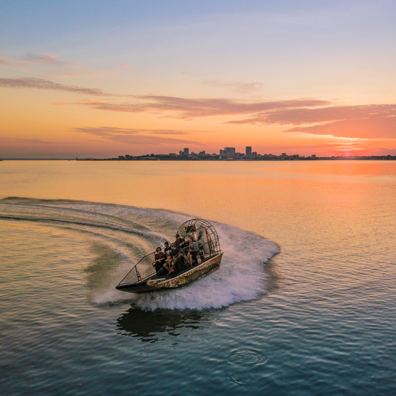An airboat glides over calm waters during a vibrant sunset