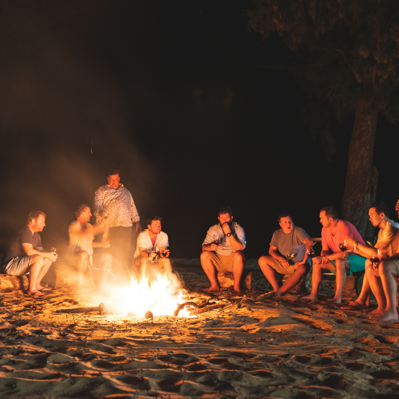 A group of people sitting around a campfire on a beach at night